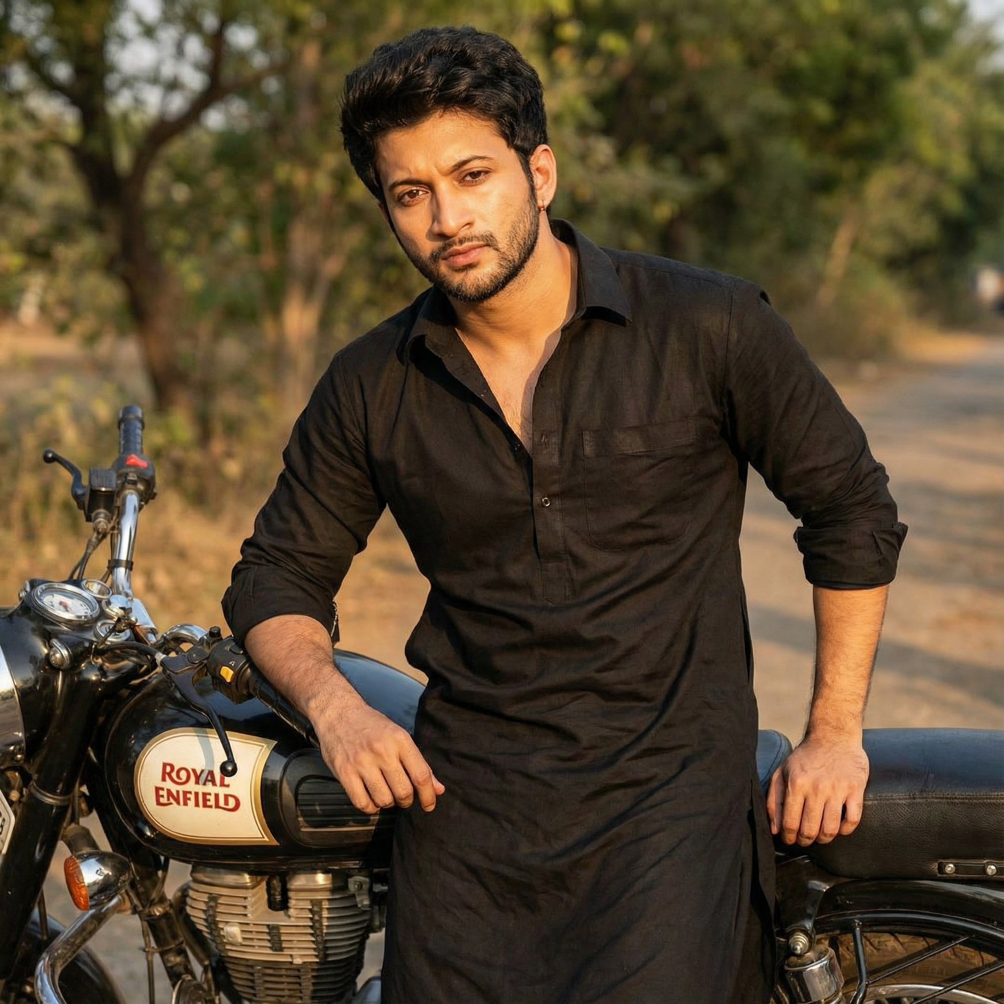 A confident portrait of a man wearing a black Pathani suit with rolled-up sleeves, leaning against a classic Royal Enfield Bullet motorcycle. He has a rugged stubble and is looking intently at the camera. Lighting: Late afternoon "golden hour" sun.