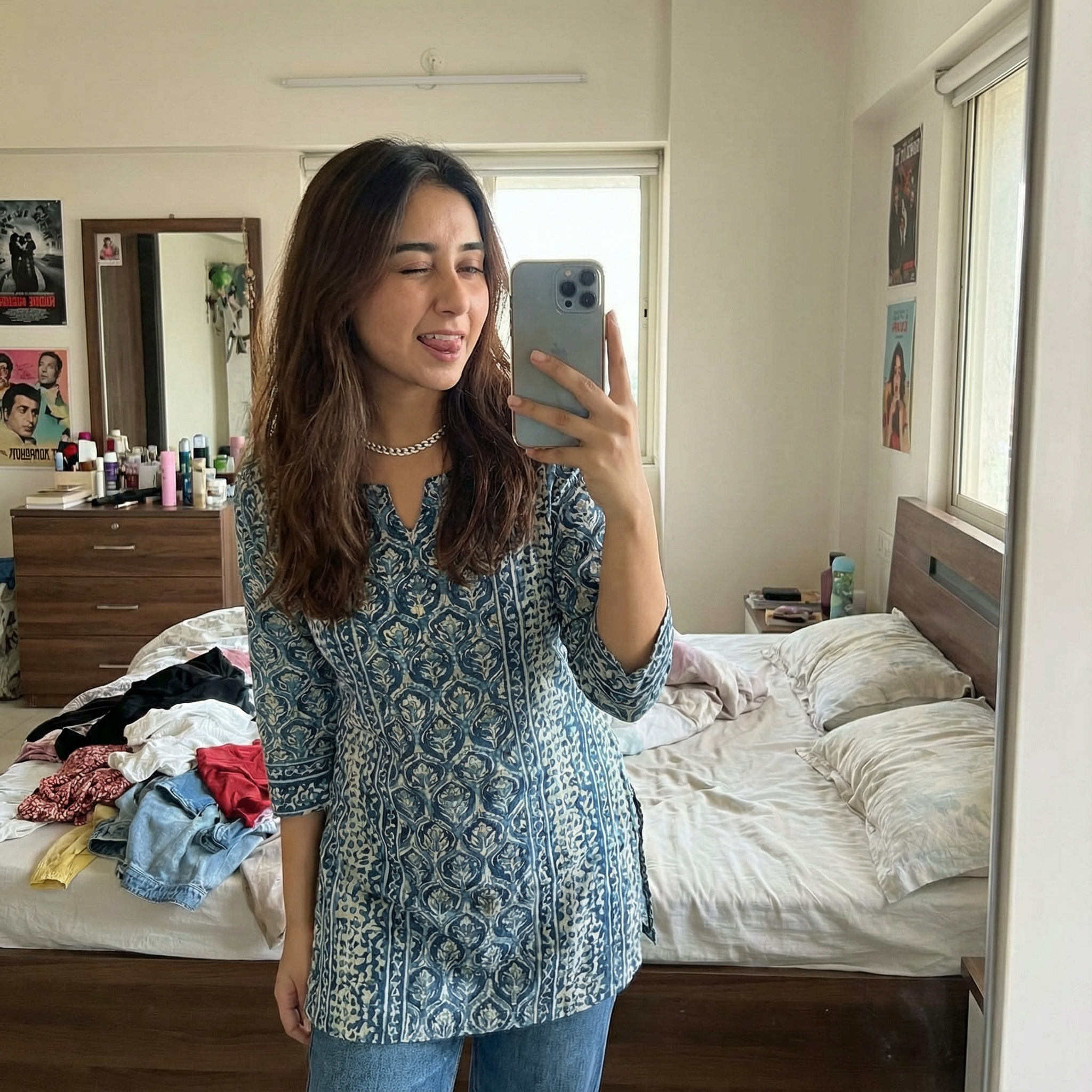 A POV shot of a girl taking a mirror selfie in her bedroom. She is wearing a cute outfit (kurta with jeans) and winking at her reflection. Expression Cue: One eye winked playfully. Tongue slightly sticking out (goofy confidence). She looks like she feels beautiful today. Background: Messy room with clothes on the bed (relatable realism).