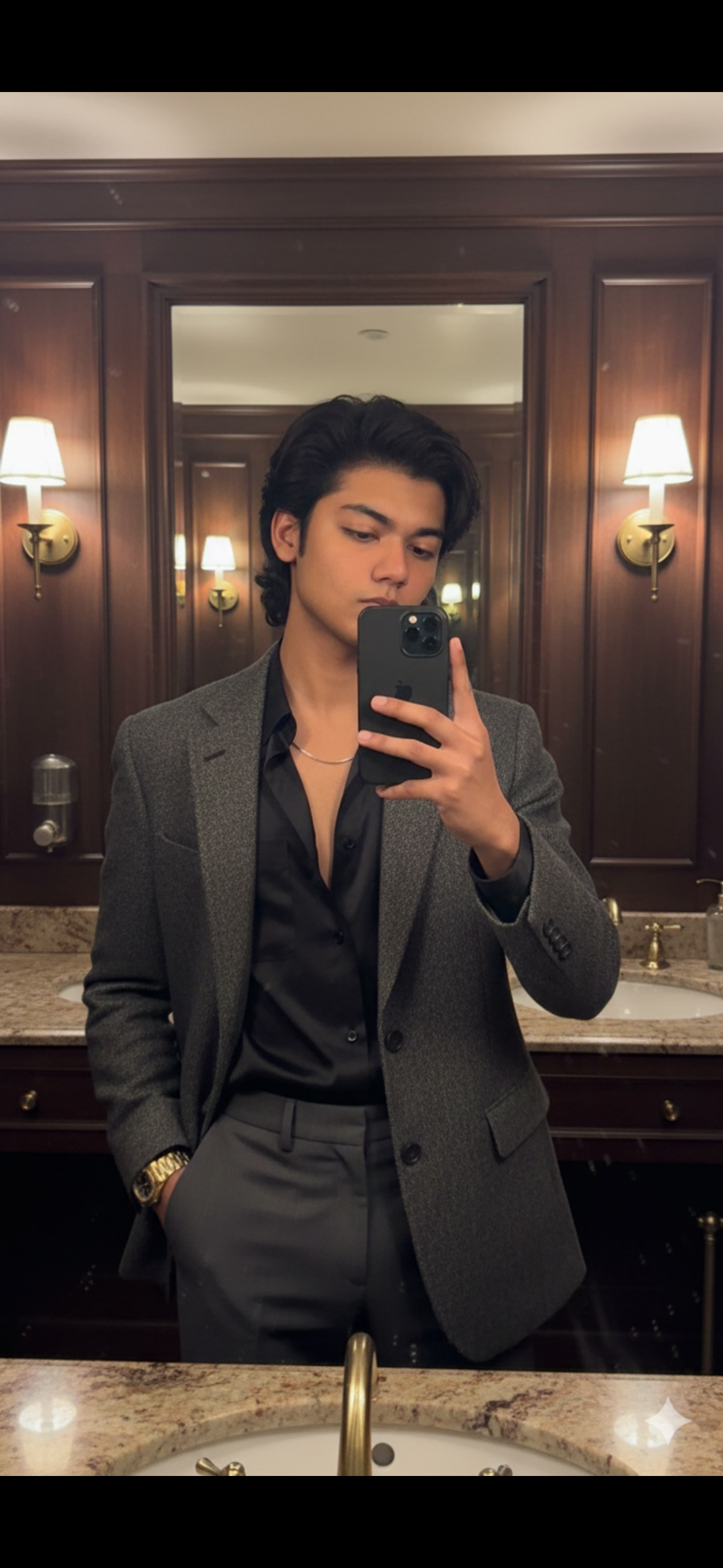 A hyper-realistic mirror selfie with I phone 17 pro Max of a young, attractive male in a vintage, dimly lit, luxurious restroom. He wears a dark tweed blazer, an unbuttoned black shirt, and high-waisted trousers, with a simple chain and oversized watch. The mood is sophisticated, moody, and timeless. 9:16 ratio.
Keep it hyper realistic 8k and keep 100% same face as the reference image.