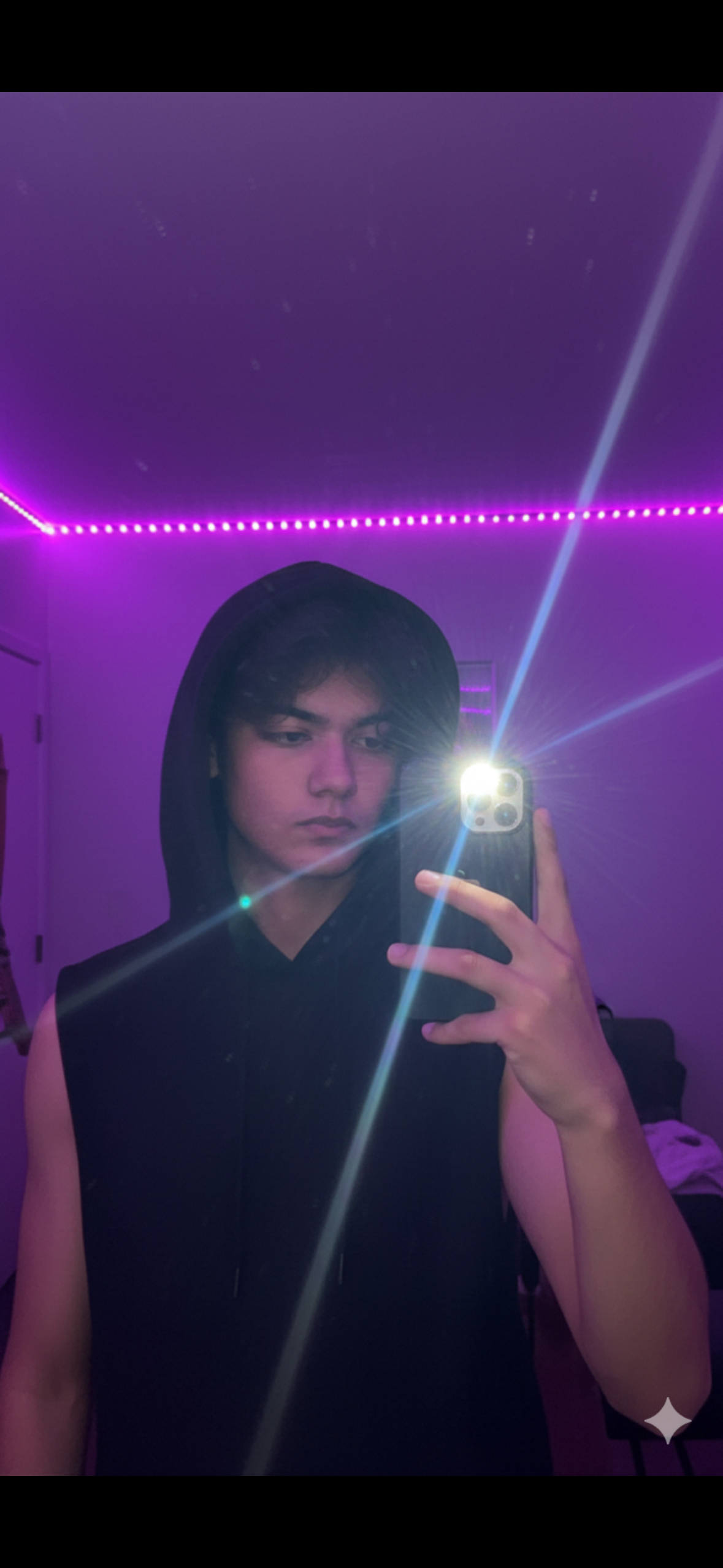 "Mirror selfie of a man in his early 17s with I phone 16 pro Max [reference face from the photo] inside a room with purple LED strip lights on the ceiling. The man is wearing a black hoodie with the hood up, has a messy hair with .
One hand is holding a phone with the flash shining brightly (starburst effect), held slightly away from his face. Behind him. Gen Z aesthetic, dominant neon purple color, lens flare. Keep it hyper realistic 8k and keep 100% same face as the reference image. 9:16 ratio.